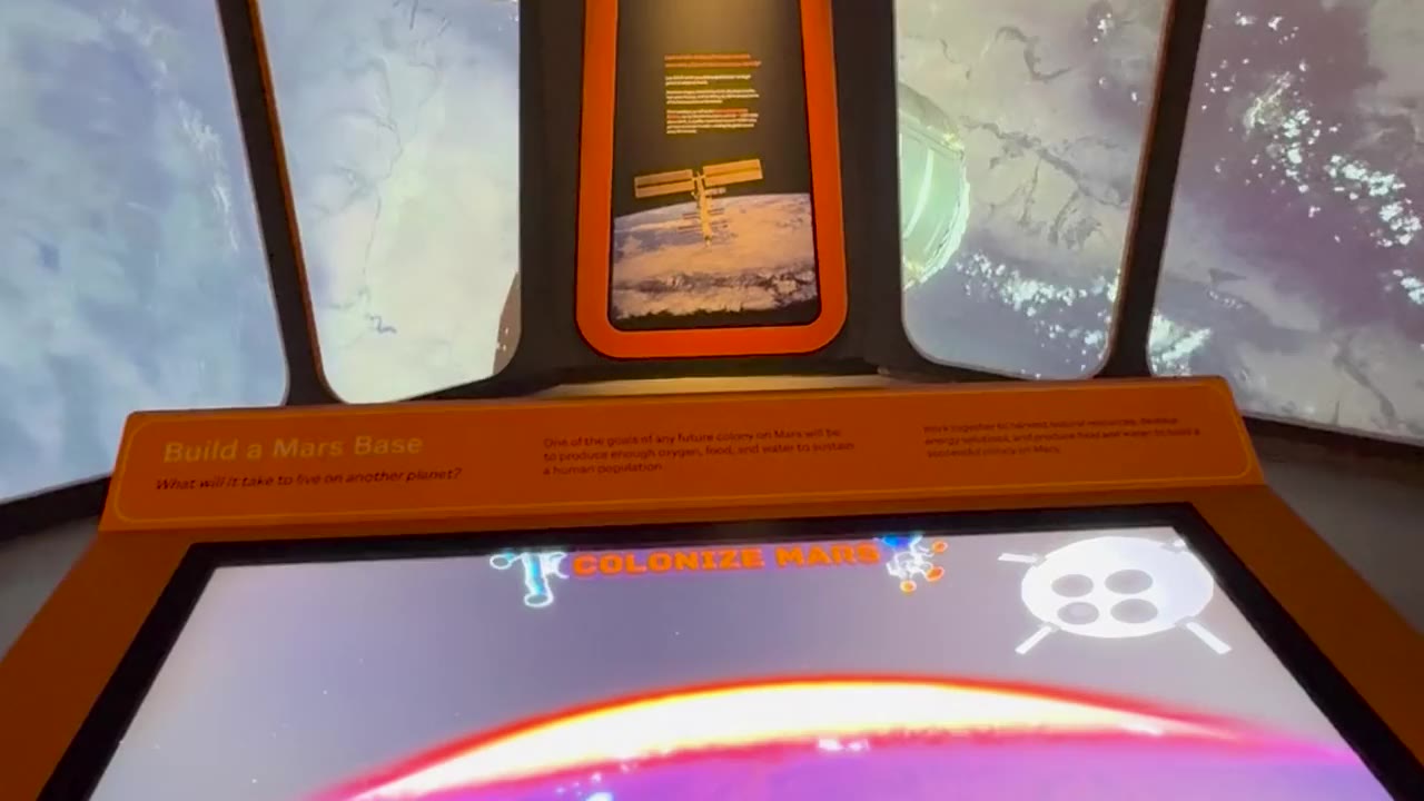 Space exhibit room: Colonize Mars touch table under Earth-orbit window screens